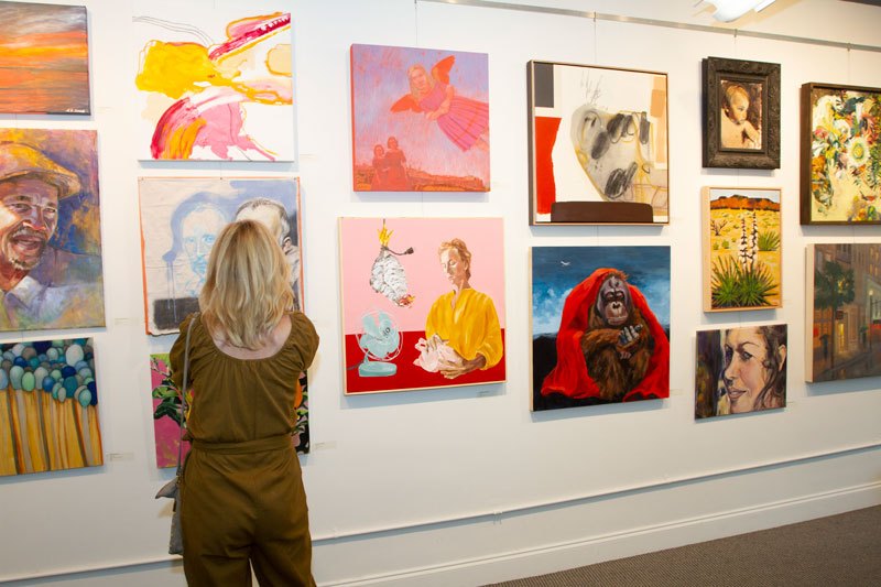 a woman looking at a wall with paintings on it