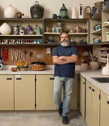 a man standing in a pottery studio with his arms crossed
