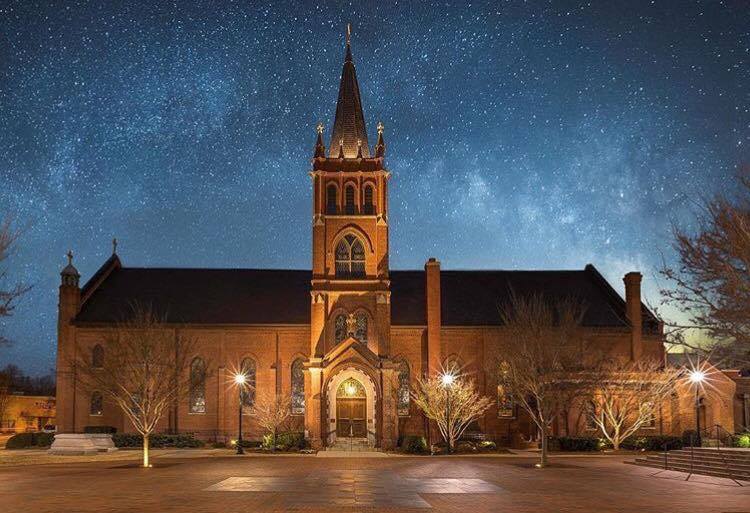 Bruton Parish Church with a tower and a courtyard with trees and a starry sky