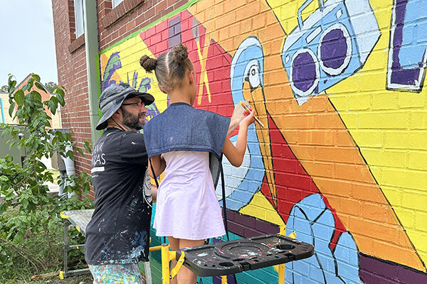 Child painting mural with adult